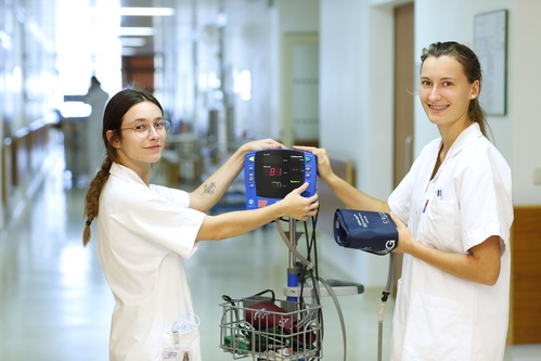 Zwei junge Frauen in der Pflege auf einem Krankenhausgang mit einem medizinisch-technischen Gerät